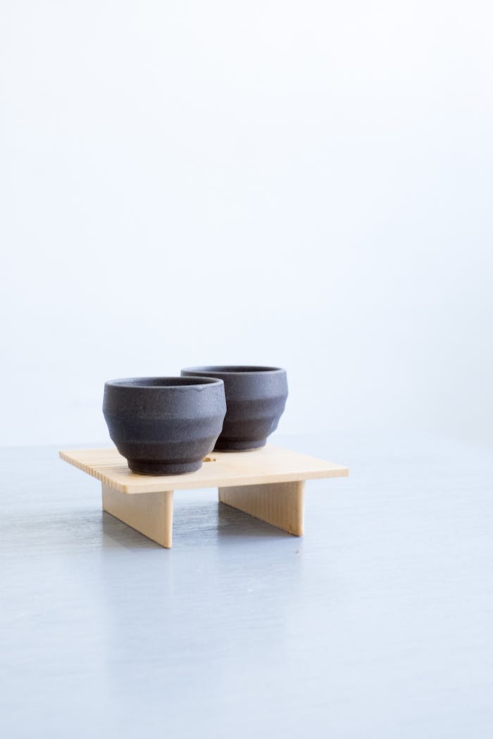 Two black ceramic cups displayed on a modern wooden stand in a minimalistic setting.
